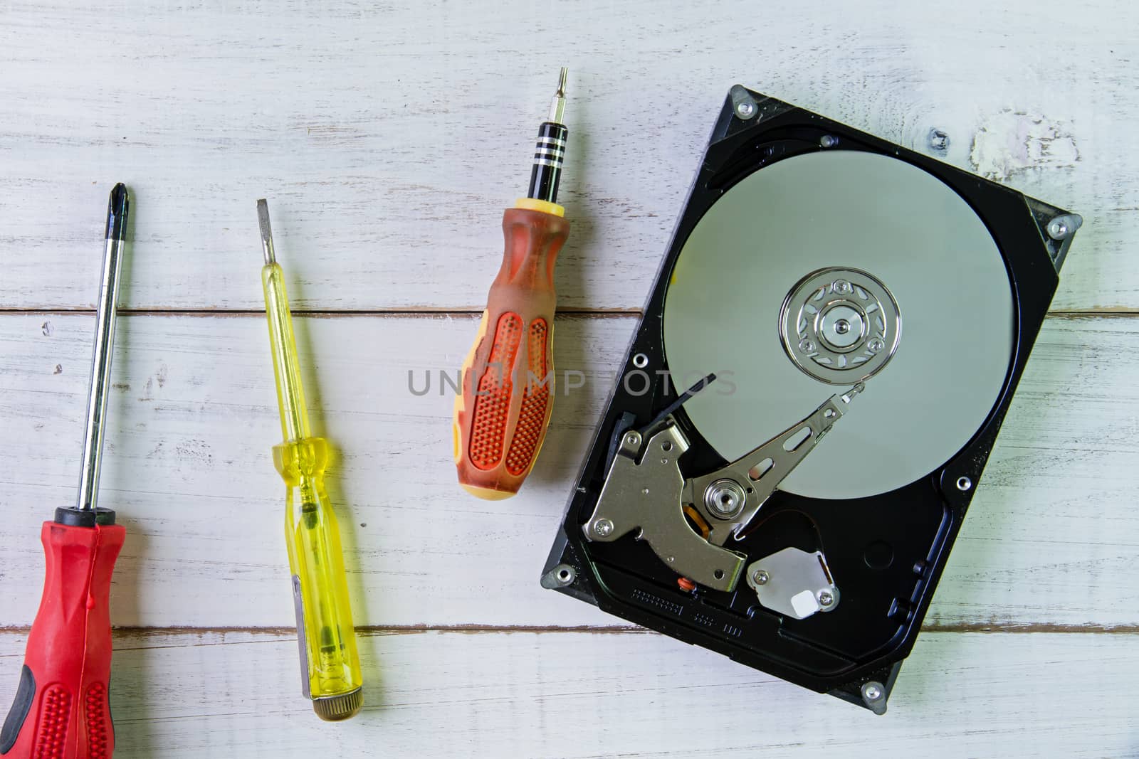 Screwdrivers and a hard disk  on the white wooden background.