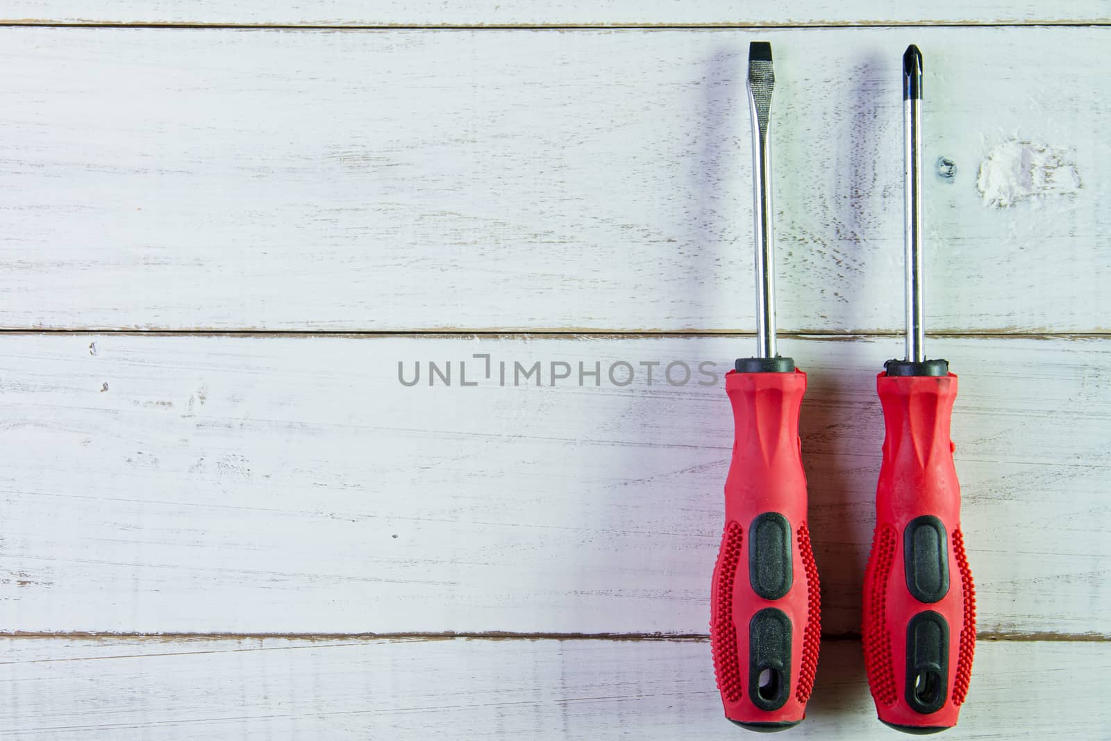 Two screwdrivers with the red handle on the white wooden background