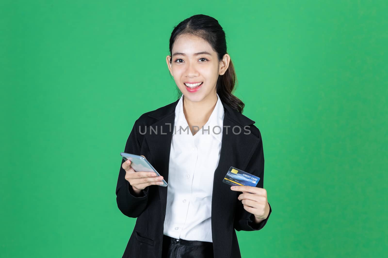 Portrait of cheerful young Asian business woman holding mobile smart phone and credit card on green isolated background. Internet of things concept.