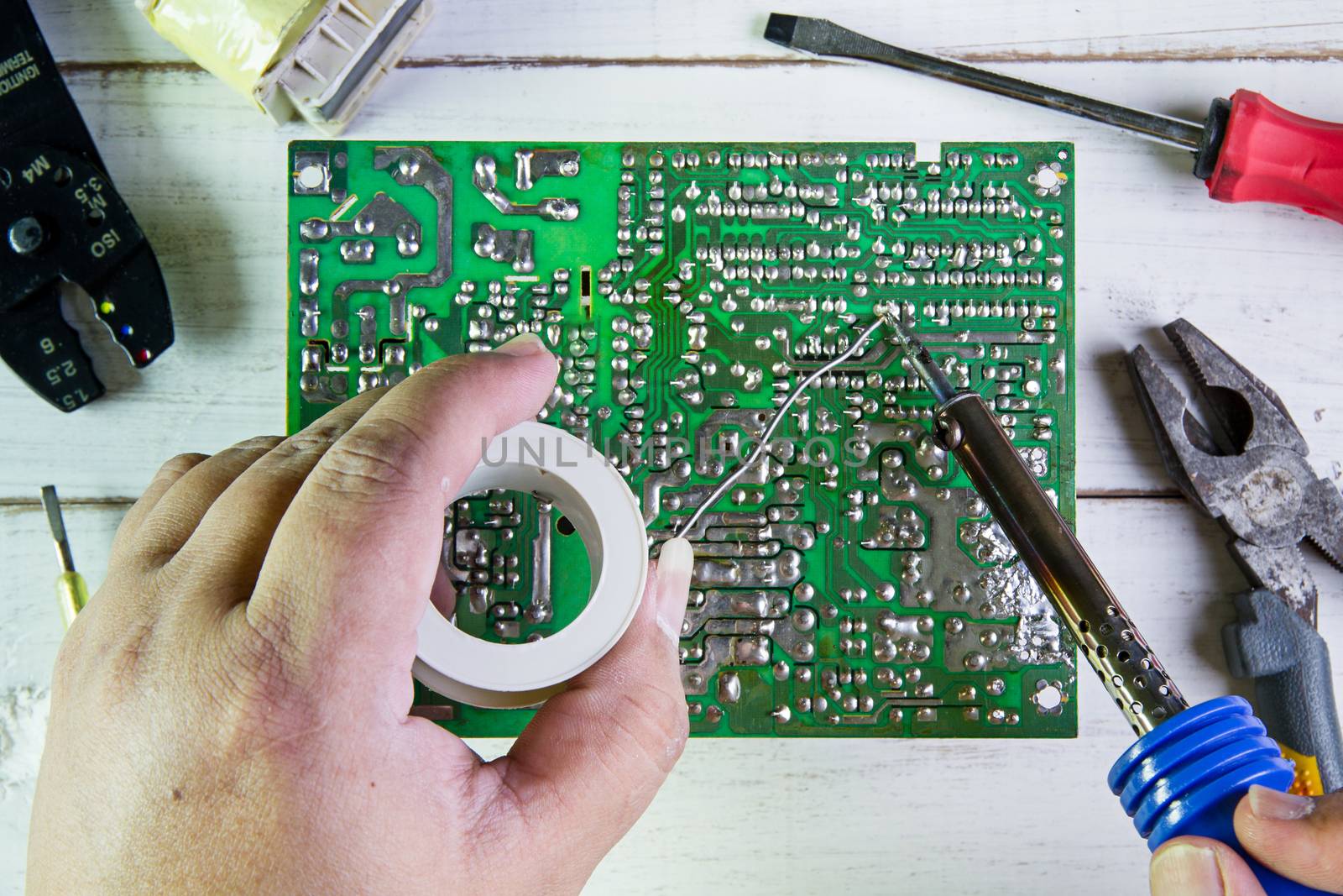 Serviceman soldering circuit board with soldering iron in the service workshop.