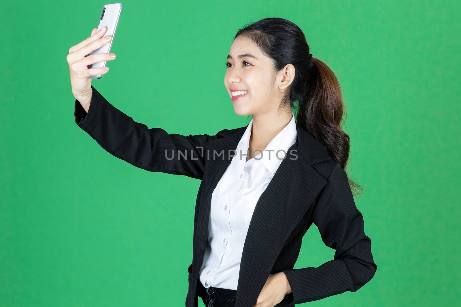 Attractive young Asian business woman taking picture or selfie with mobile smart phone on green isolated background.