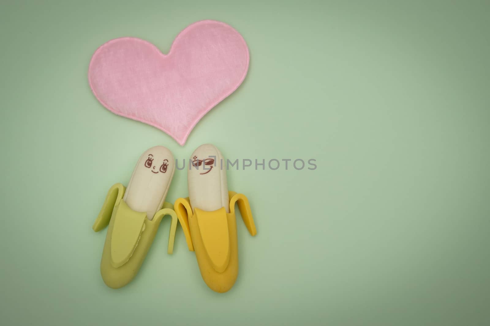 Two rubber banana and heart-shape pillow on green background, valentine concept.