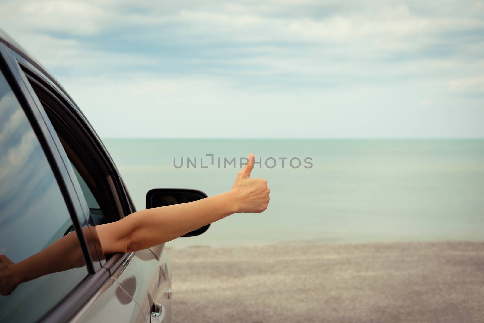 Happy woman raised arms from the car parked in the sea on a bright day. Vintage picture.