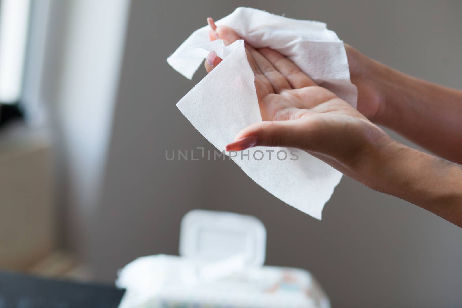 Woman with long nails clean hands with wet wipes, blurred package in background