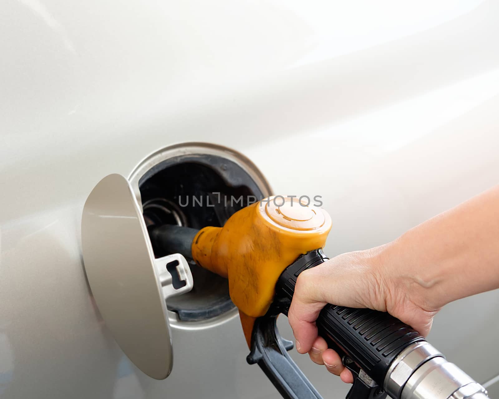 The gold car is filling the fuel at the oil station. Hand holding Fuel nozzle in gas pump.