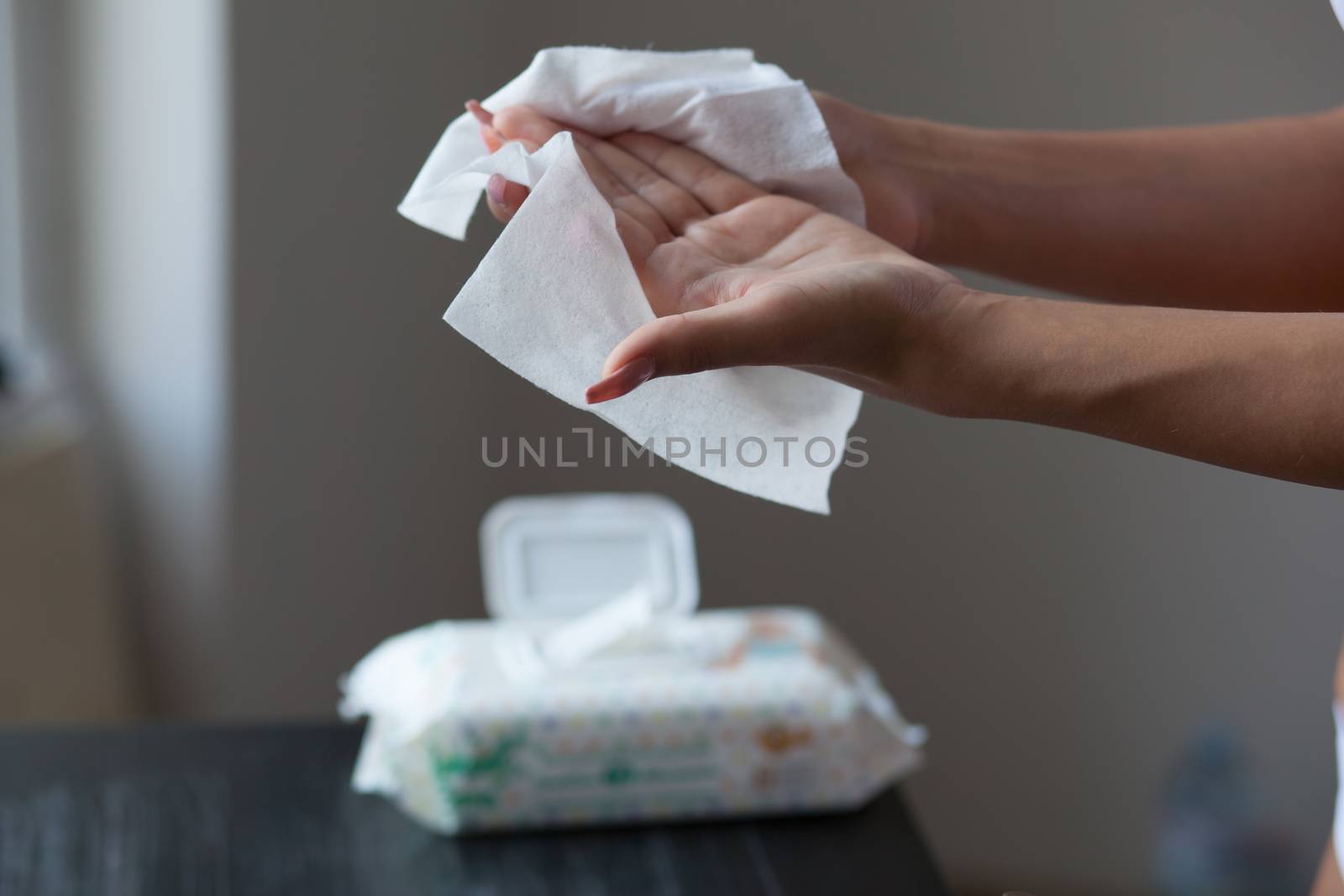 Young woman clean hands with wet wipes, blurrer package in background