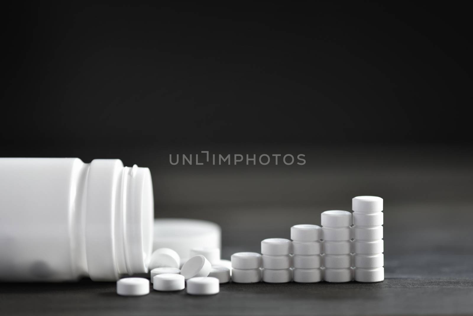 White medical pills and tablets spilling out of a drug bottle. top view with copy space. On Black wood Background. Natural herbs, organic pills, vitamins from medicinal plants. Alternative medicine. 