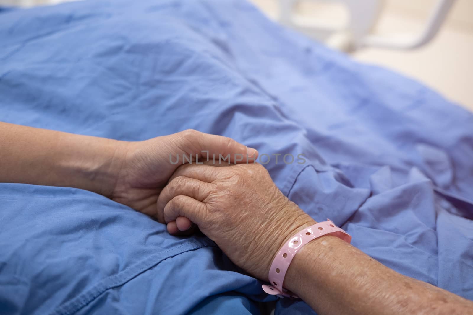 The hand of the woman is holding mother's hand that sleeping in the hospital bed.