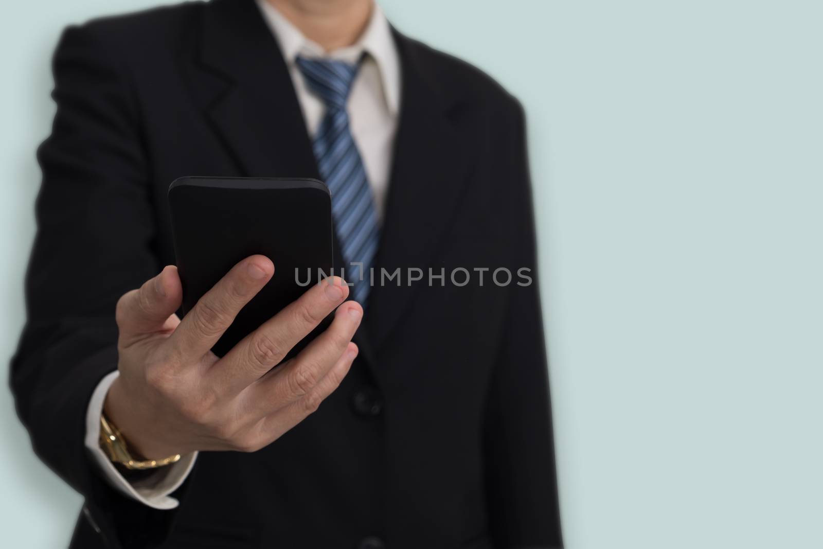 Businessmen in suit holding mobile phone on blue background with copy space.