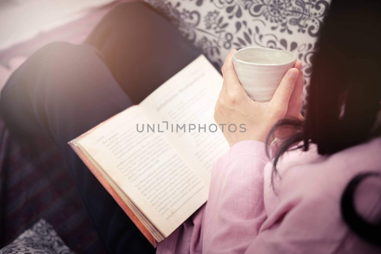 Woman reading a book and holding cup of coffee in the morning.