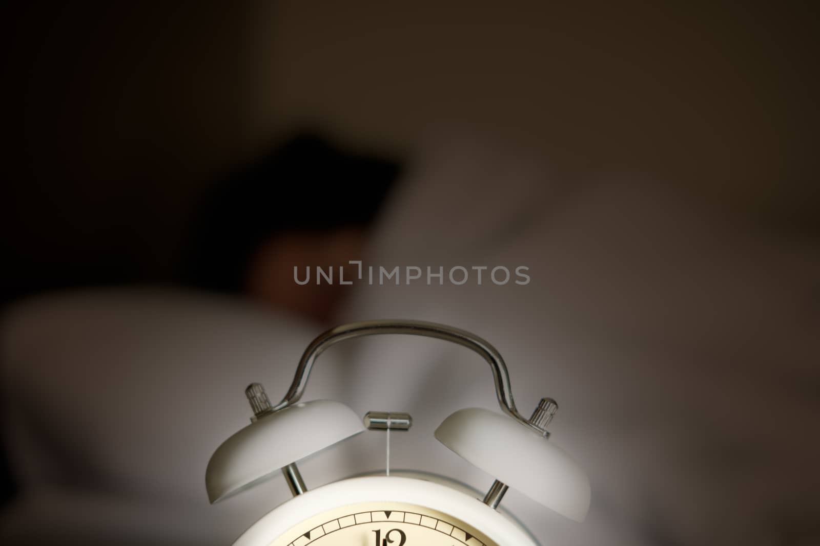 A glowing alarm clock is placed in front of a sleeping woman.