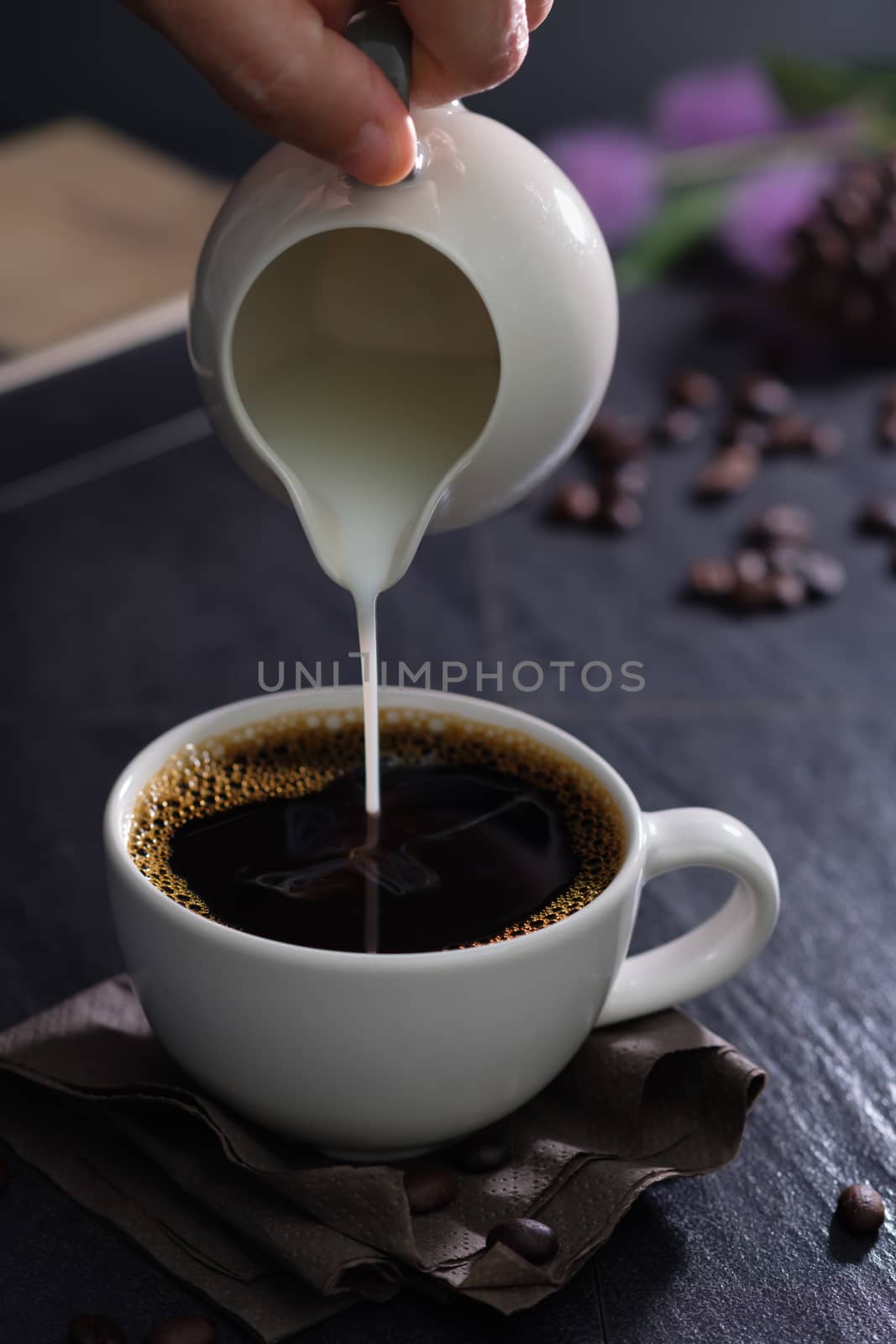 Classic still life with The hand is pouring milk to a cup of coffee with copy space, verticle picture.