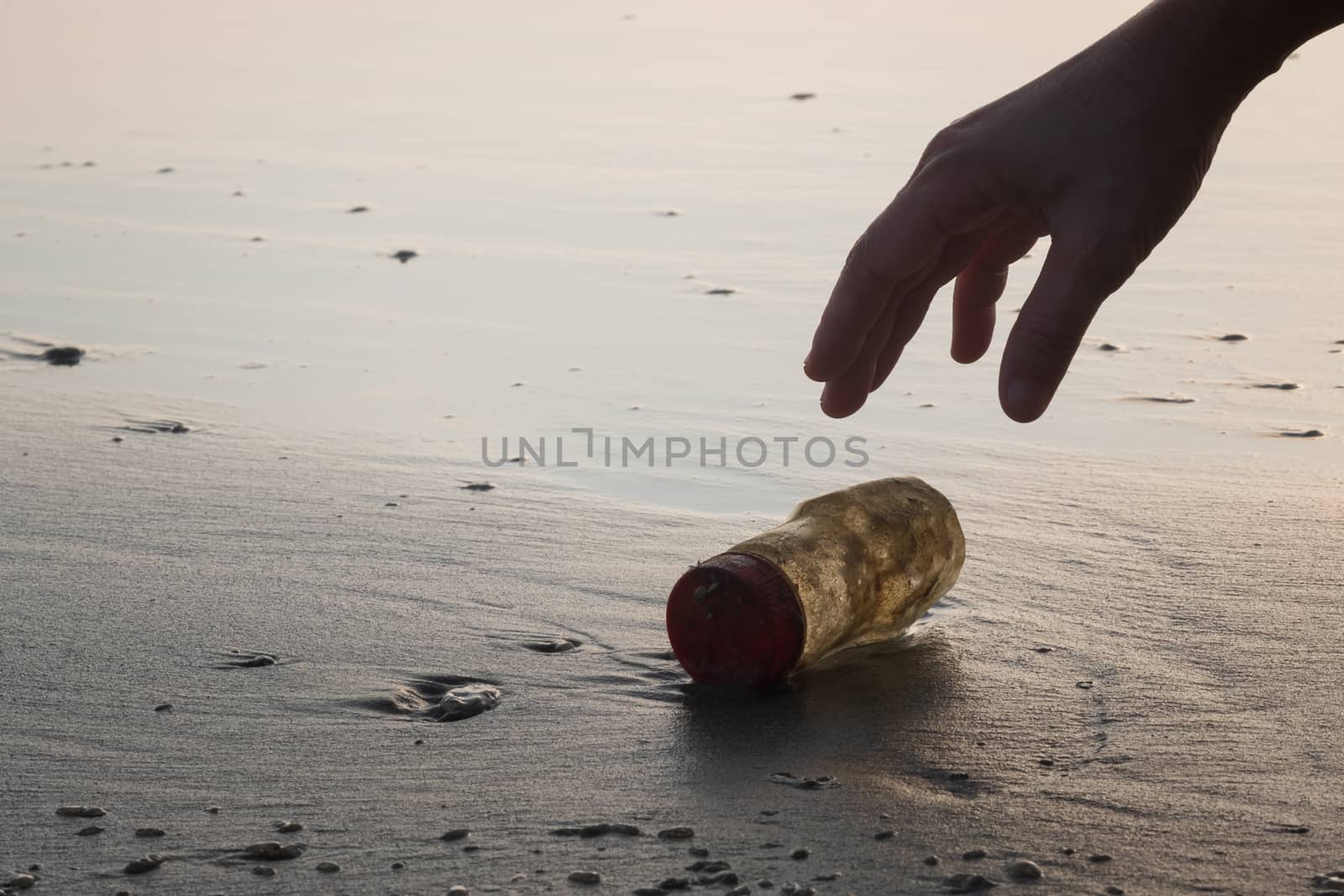 The hand of a woman is picking up a plastic bottle to clean the beach.