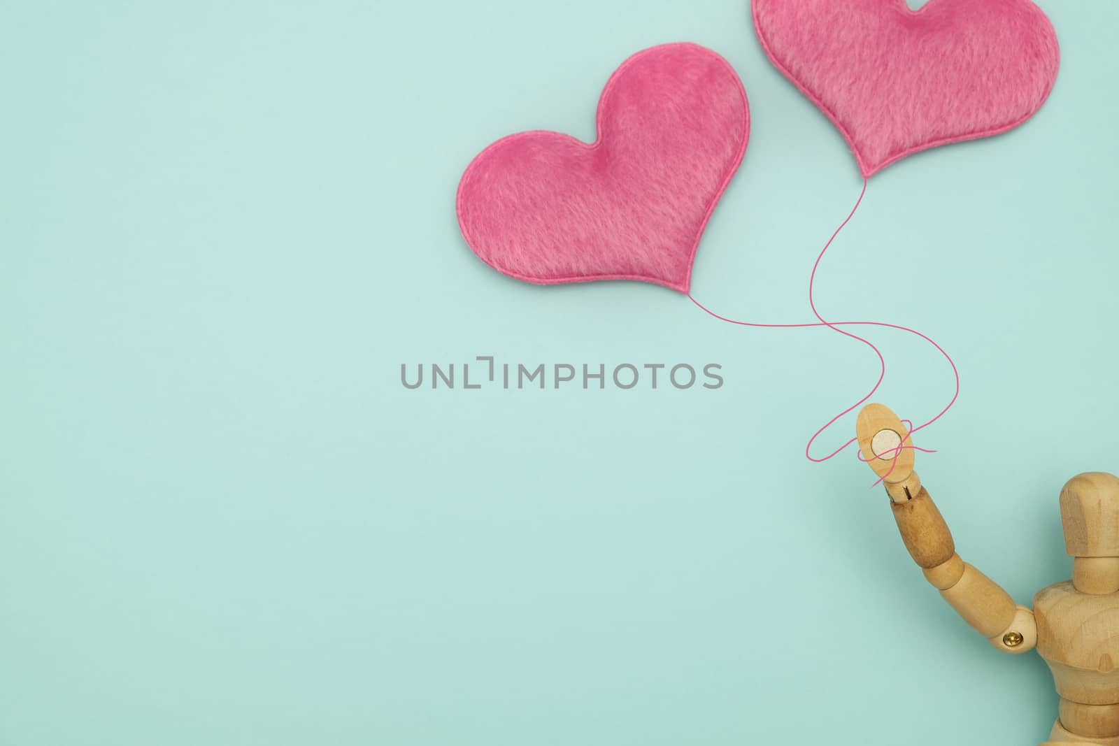 Wooden dummy, holding a heart-shaped balloons on blue background with copy space for write and valentine concept.
