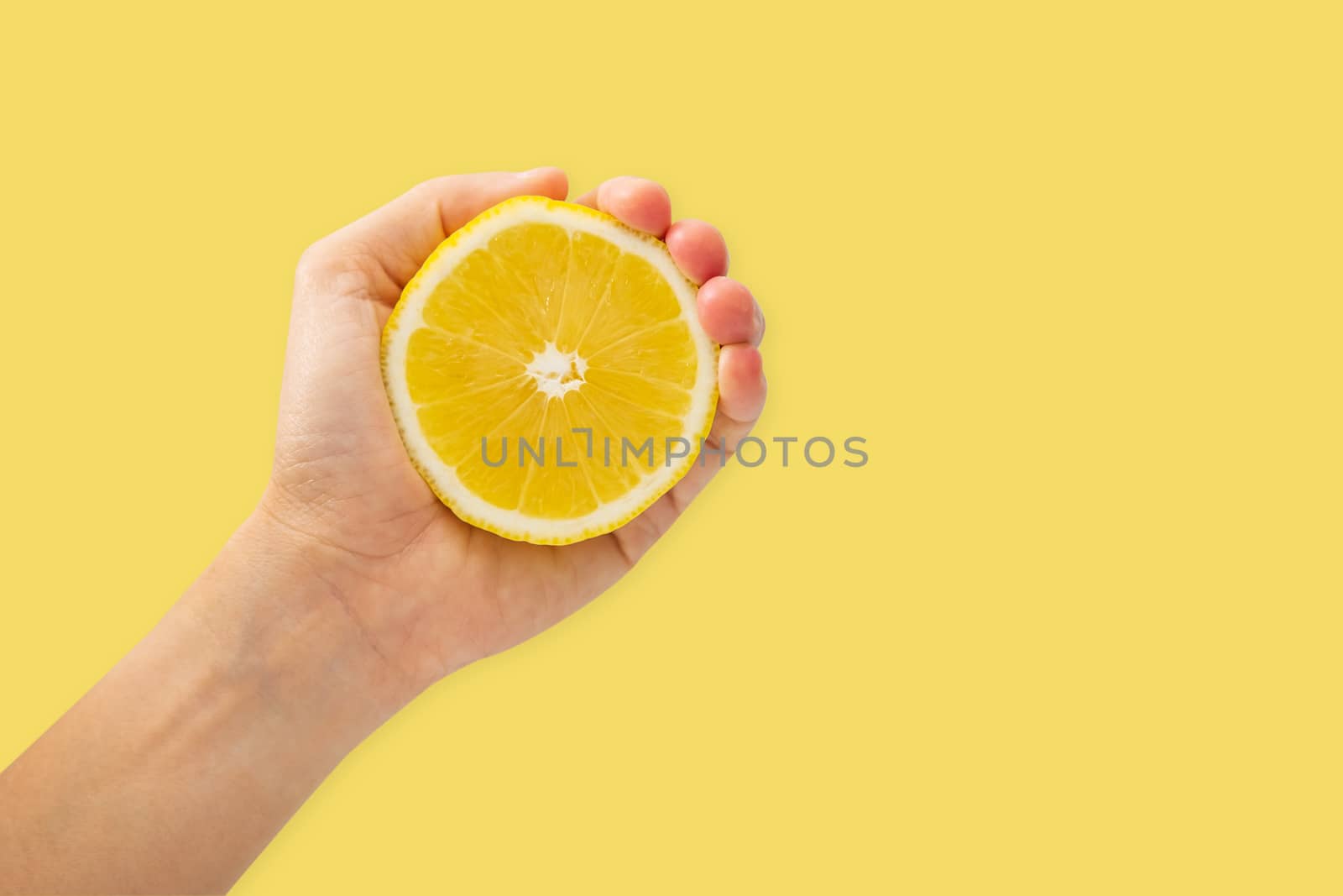 Female hand squeezing half of lemon on yellow background by feelartfeelant
