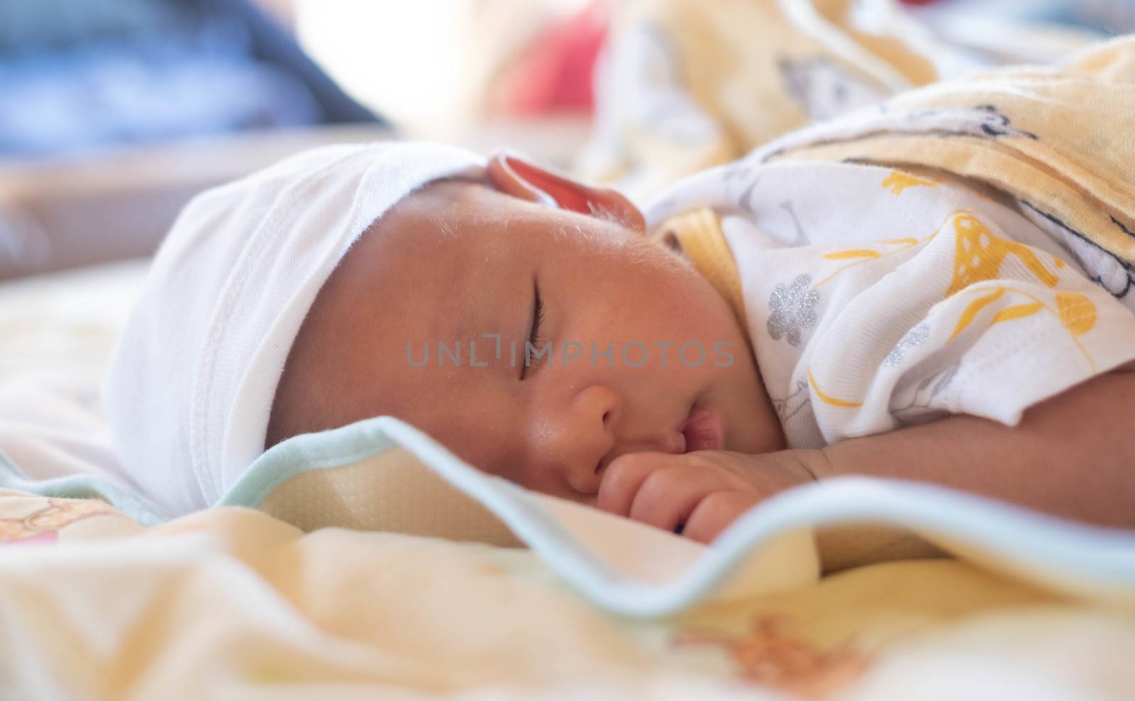 portrait of cute little baby infant  boy wearing white hat lay to sleep prone on the bed, a yellow blanket in his room ,