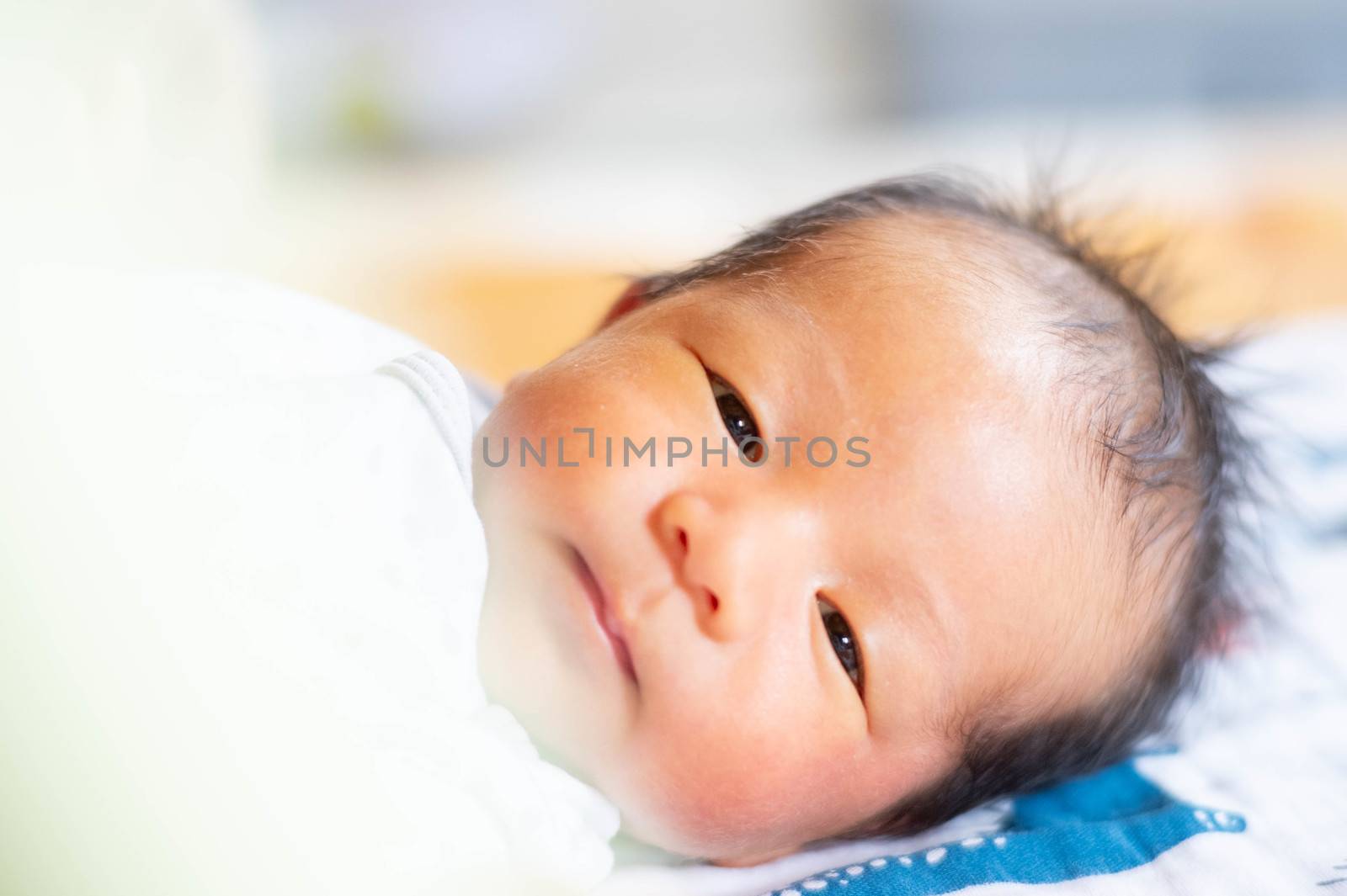 Portrait Photo of happy newborn baby infant with big black eyes lay down on the bed