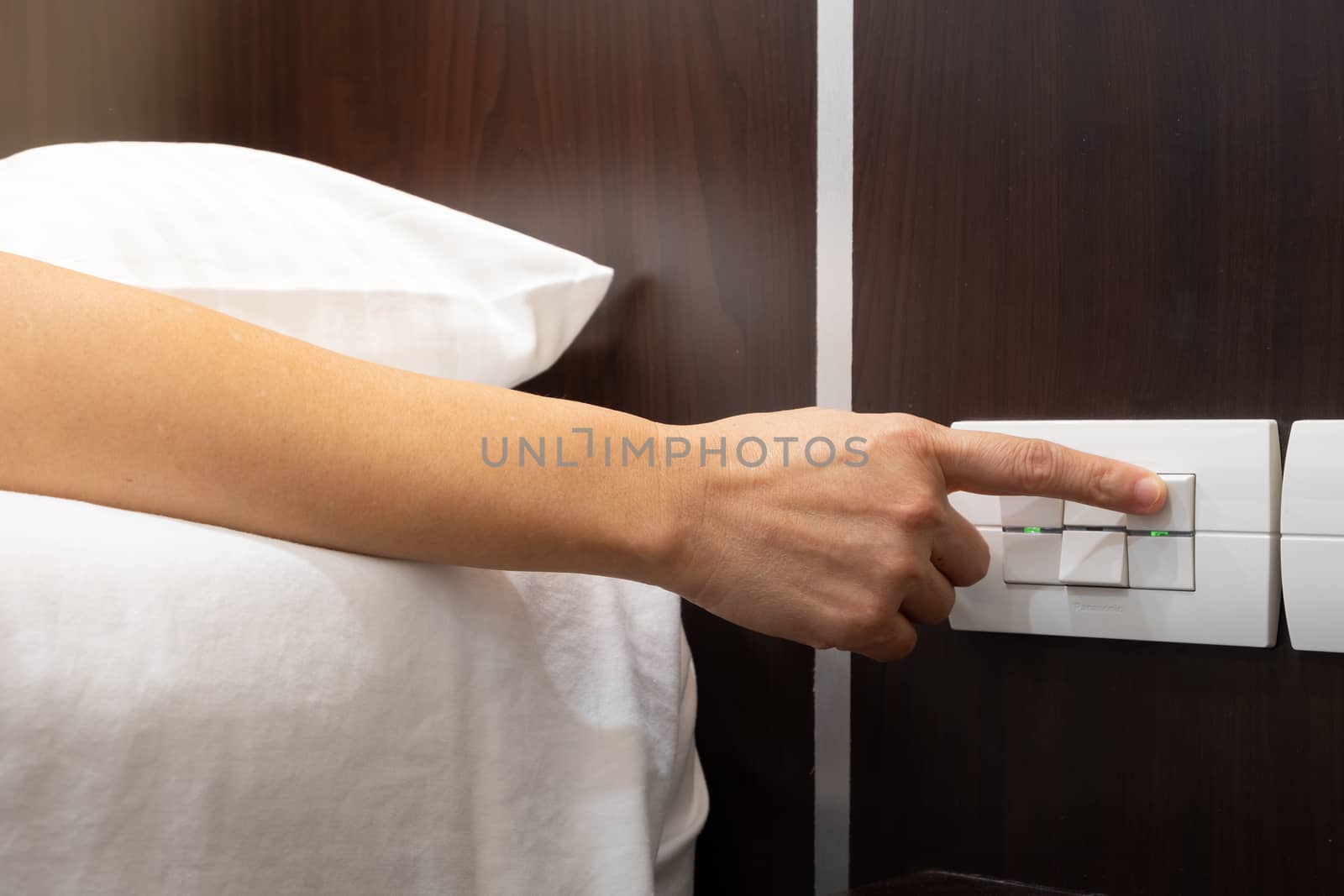 Hand turning "on" or "off" on light switch near the bed in the h by feelartfeelant