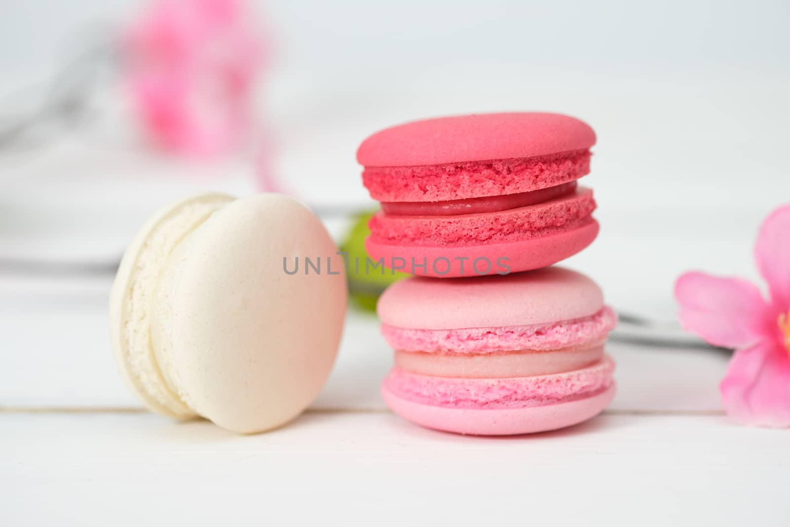 Macaroons and flowers on the white wooden background.