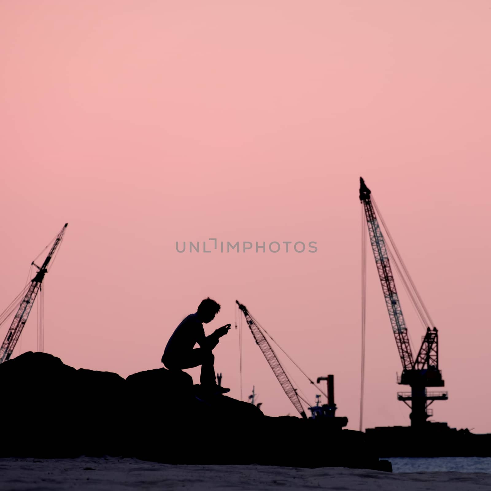 silhouette image of a man sitting in front of a book reading alone by the sea on pink background.