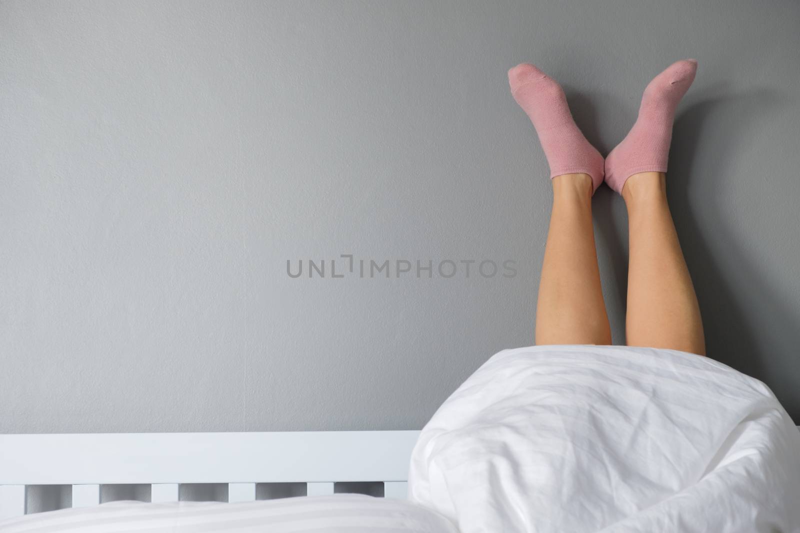 Good morning by stretching feet with pink socks out of the blanket. Choose focus point with copy space.