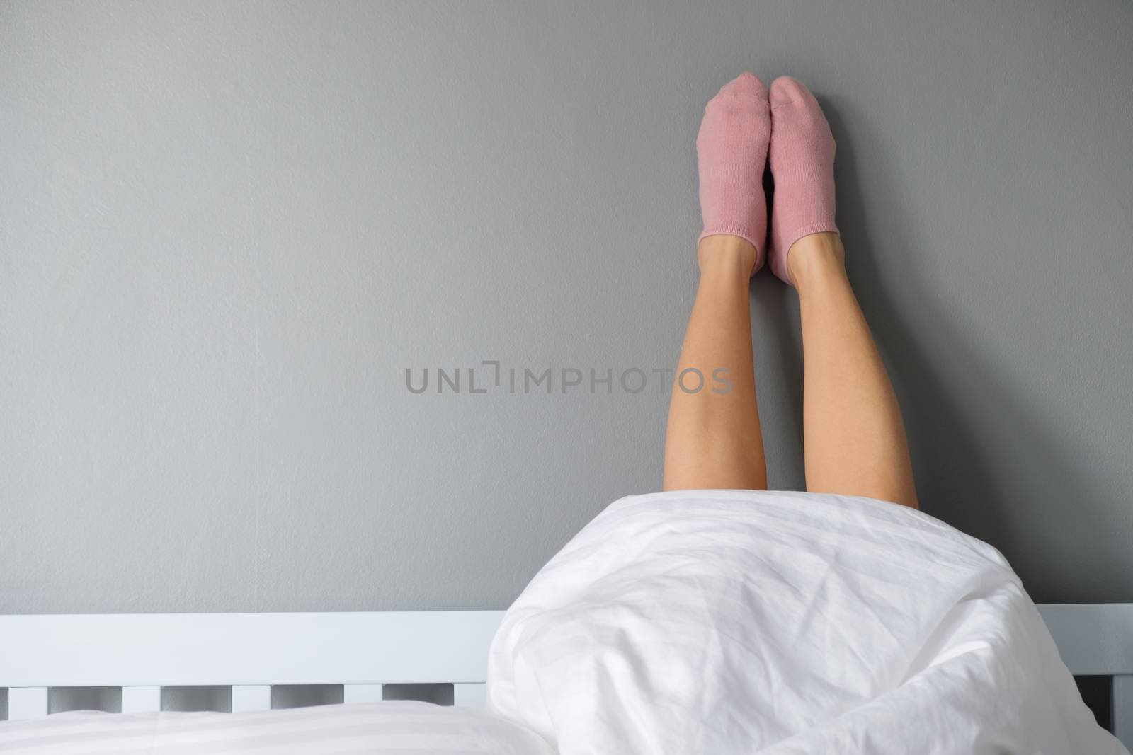 Good morning by stretching feet with pink socks out of the blanket. Choose focus point with copy space.