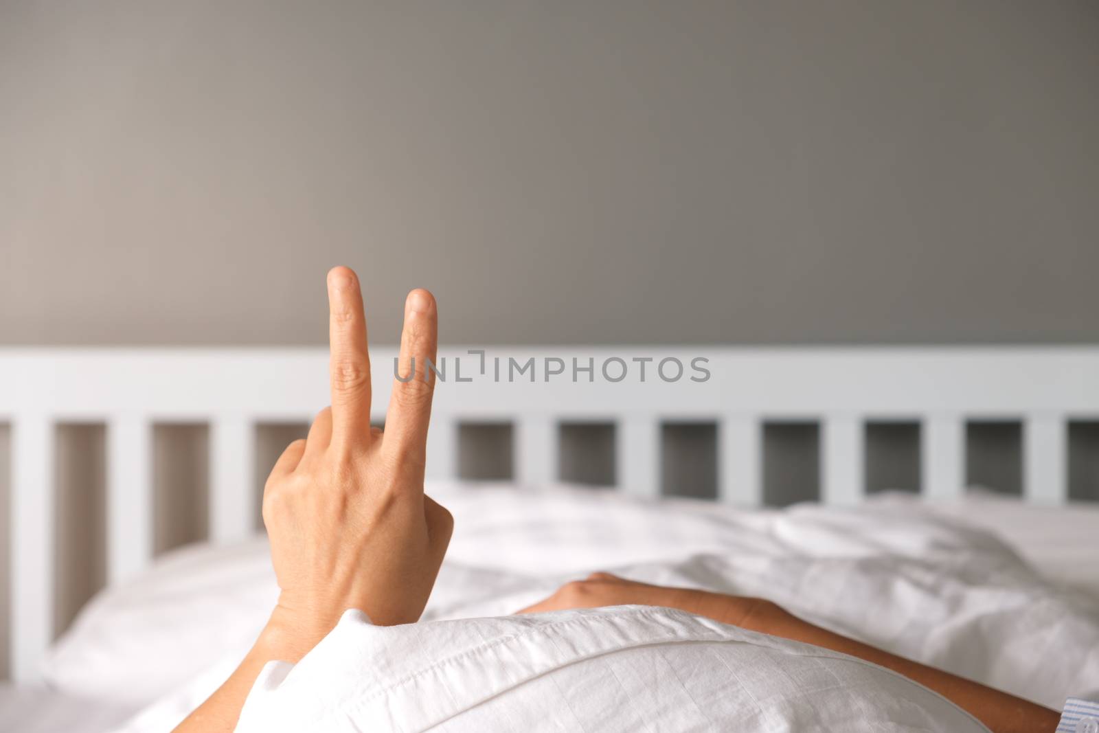 Woman raising two fingers up on hand on the bed show that you should welcome the new morning.