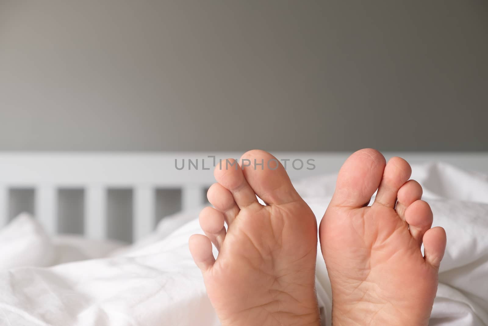 The feet of a woman lying on a white bed in the morning.