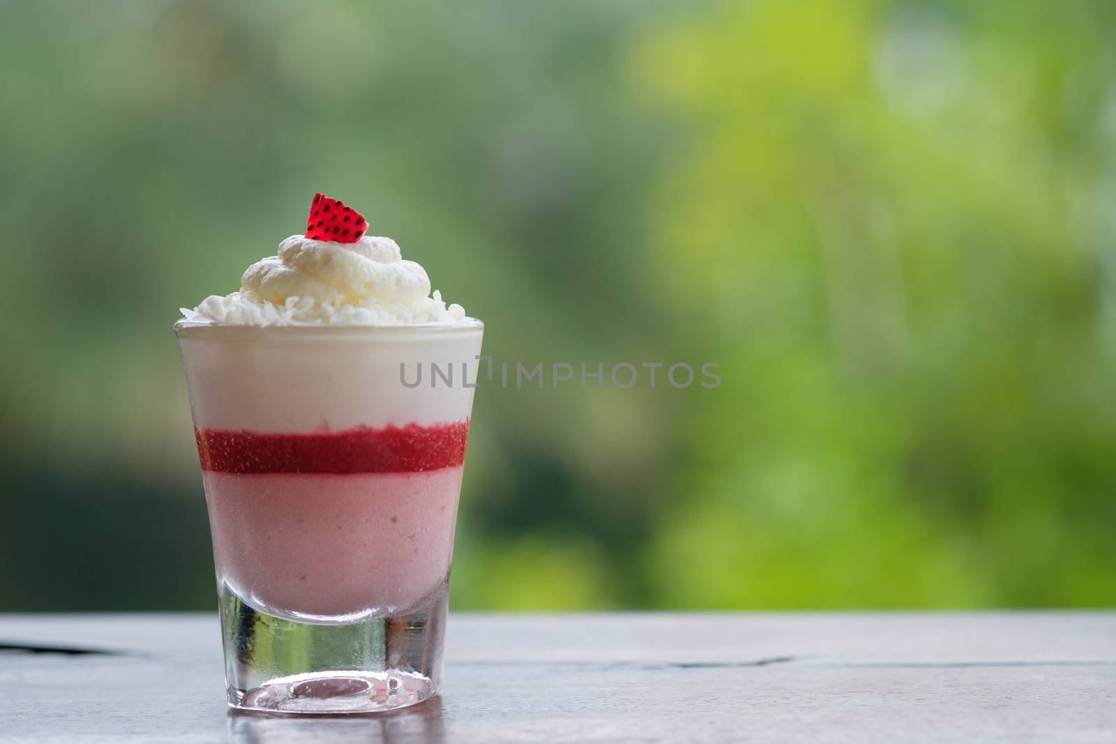 Strawberry mousse cake in a small glass placed on a wooden table in bokeh background with copy space.