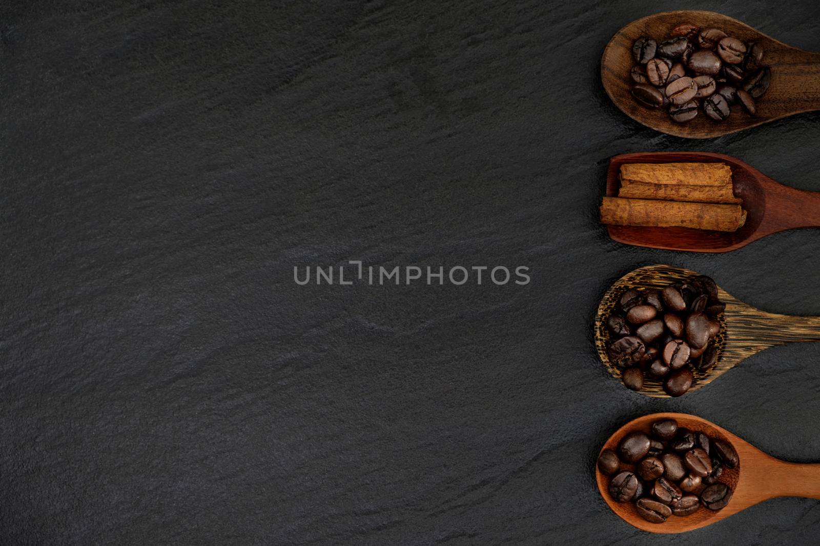 Roasted coffee beans  in wood spoons on rustic black background