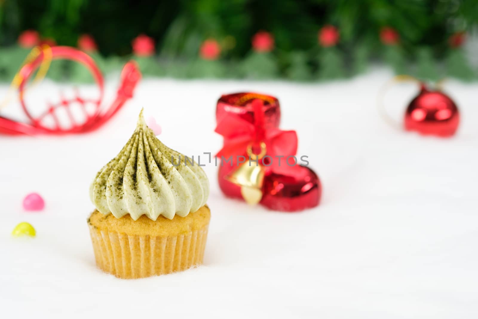 Christmas Cupcake with small red boots, Sprinkle candy in many colors around, fir tree background.