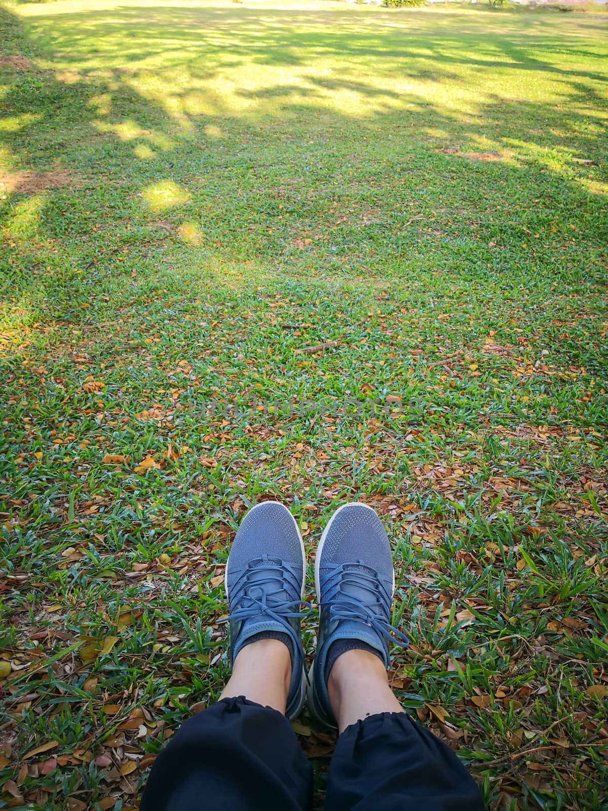 Woman's legs in grey shoes sit on dry leaves in the park.