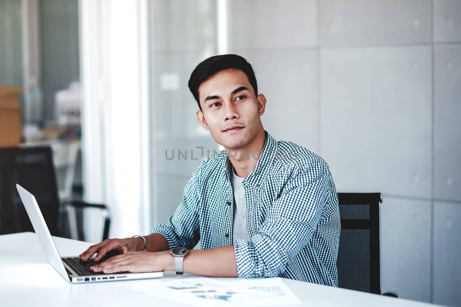 Happy Young Businessman Working on Computer Laptop in Office. Smiling and looking away