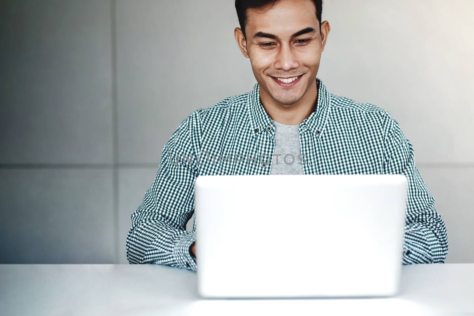 Happy Young Businessman Working on Computer Laptop in Office. Smiling and looking at Computer Screen