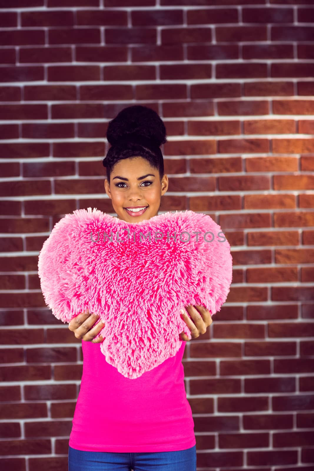 Portrait black hair model holding a pink heart shaped pillow on a red brick wall