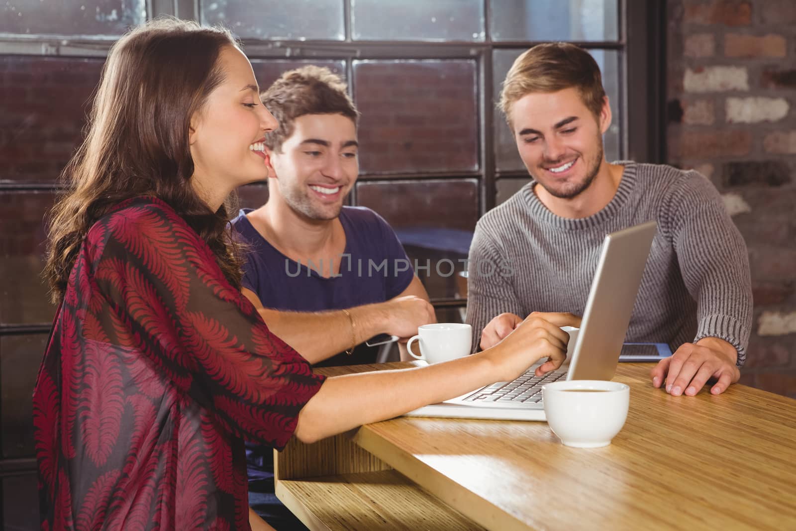 Smiling friends having coffee together and looking at laptop at coffee shop