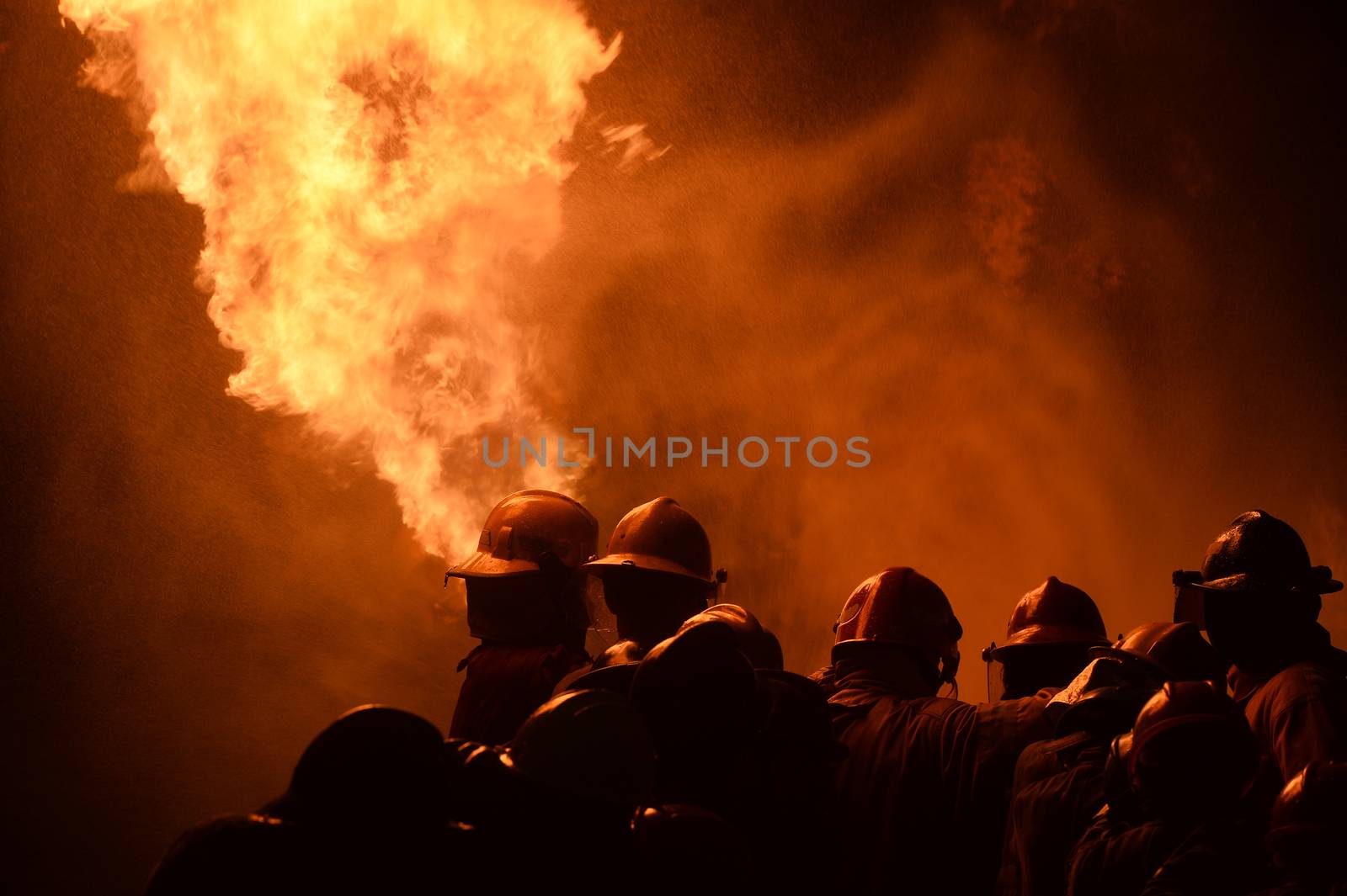 firefighters with fire hose fight with fire at night