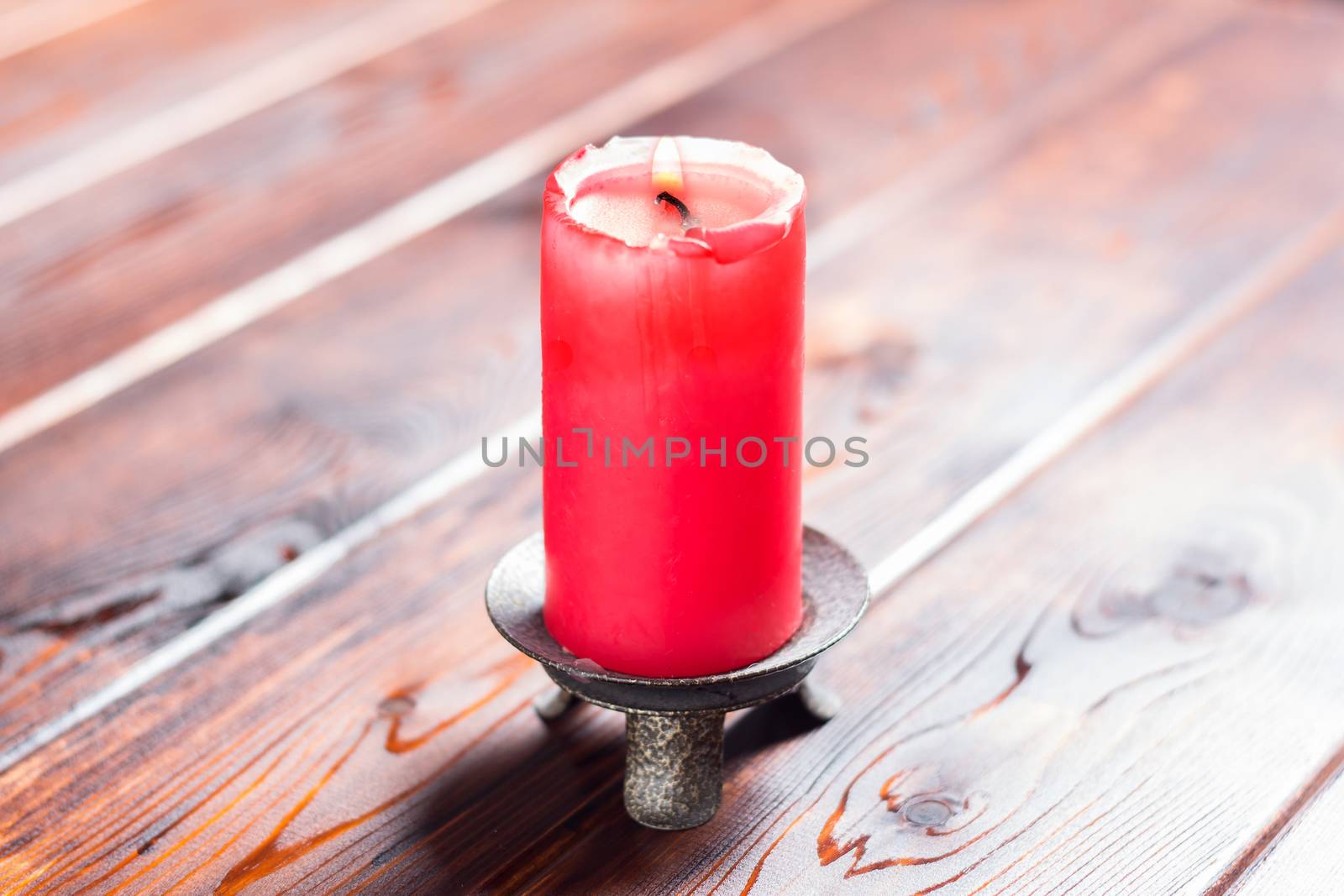 burning old candle with vintage brass candlestick on wooden background in minimalist room interior with copy space. A burning candle stands on a wooden table. A red lighted candle