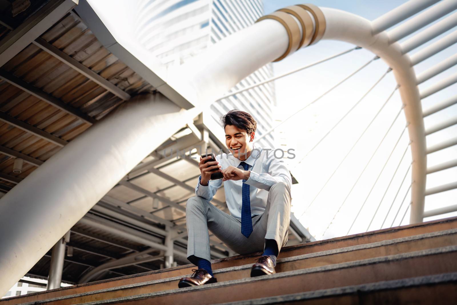 Happy Young Businessman Sitting on Staircase and Using Smartphon by Black-Salmon