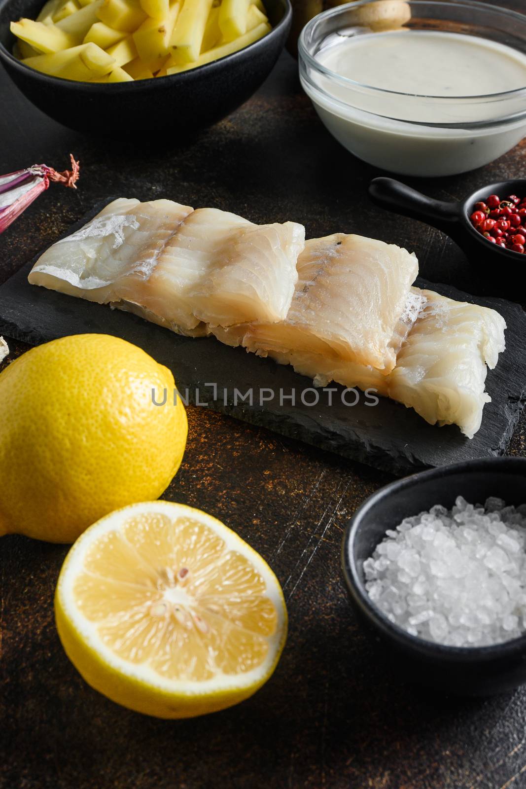 British traditional fish and potato chips ingredients raw fish fillet, beer batter, potatoe, shallotgarlic, salt, peppercorns on rustic metal textured surface or table side view by Ilianesolenyi