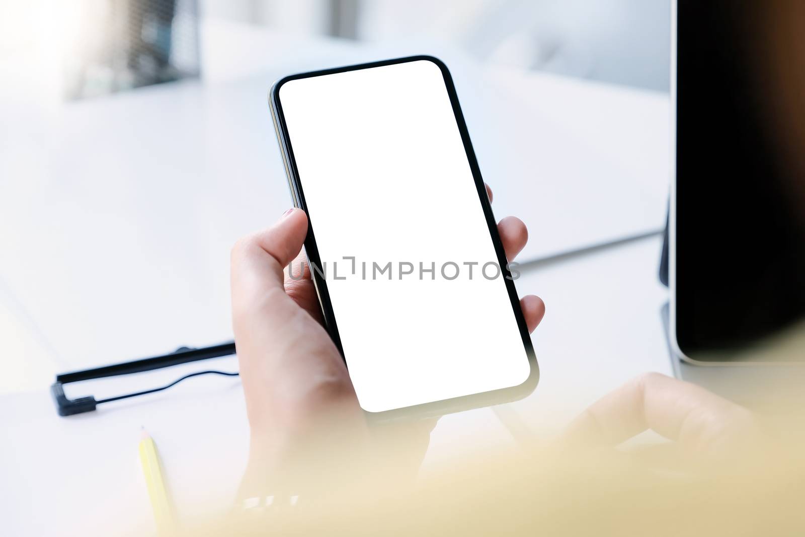 Woman hand holding smartphone on workplace. Blank screen mobile phone for graphic display montage.