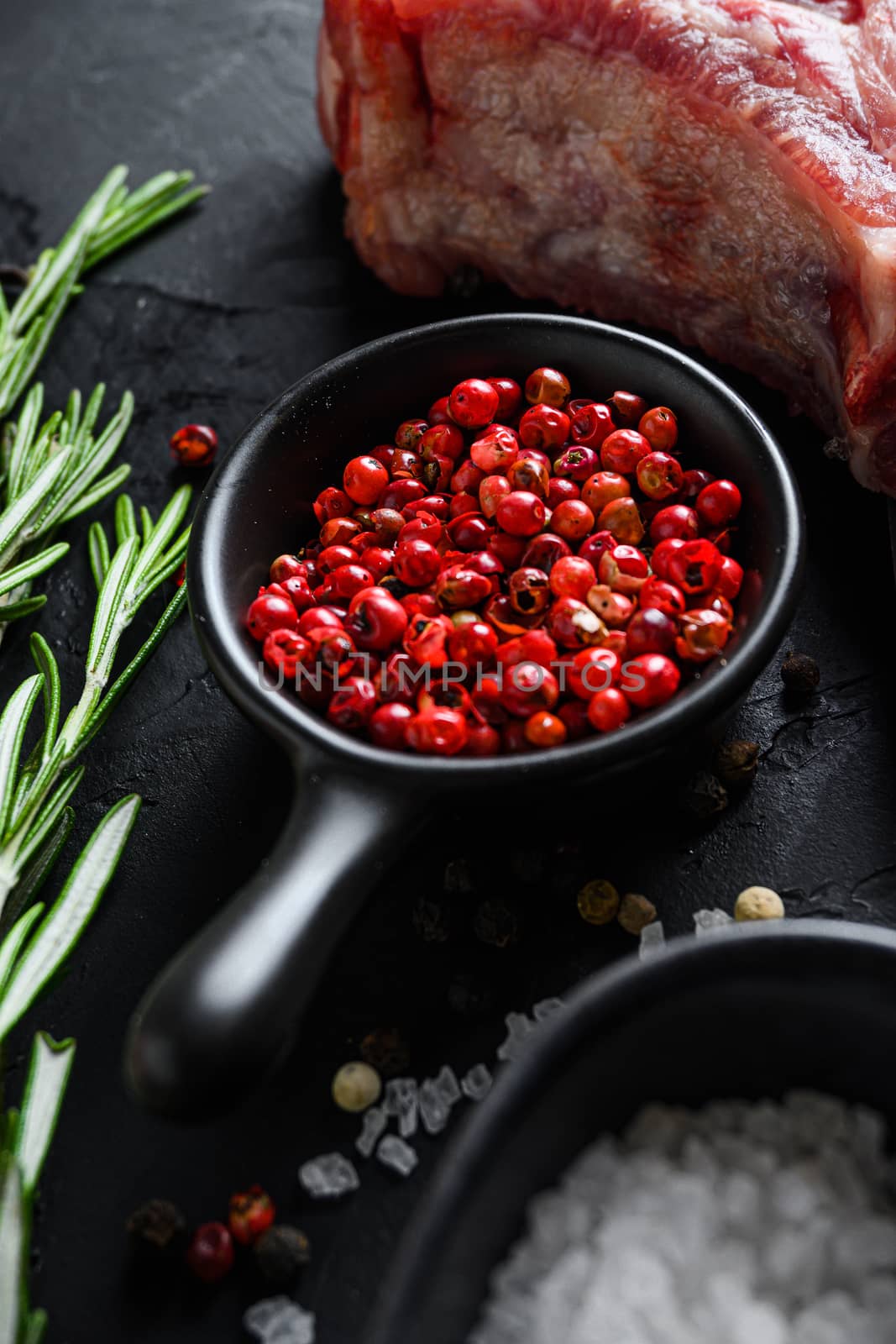 Rose Peppercorn and Rosemary herbs close up on black stone table with spices and raw meat near side view selective focus vertical. by Ilianesolenyi