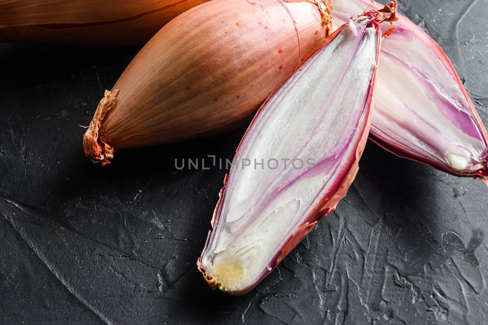 Shallot, eschalot or scallion raw ripe onions sliced and halved black background top view close up horisontal.
