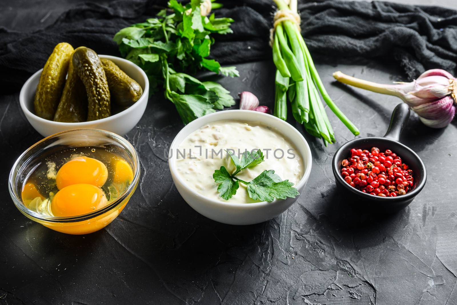 Sauce Tartar with pickles wwith ingredients eggs green onions pickles, capers, dill, parsley, garlic, lemon . Sauce boat on a black concrete textured background side view close up by Ilianesolenyi