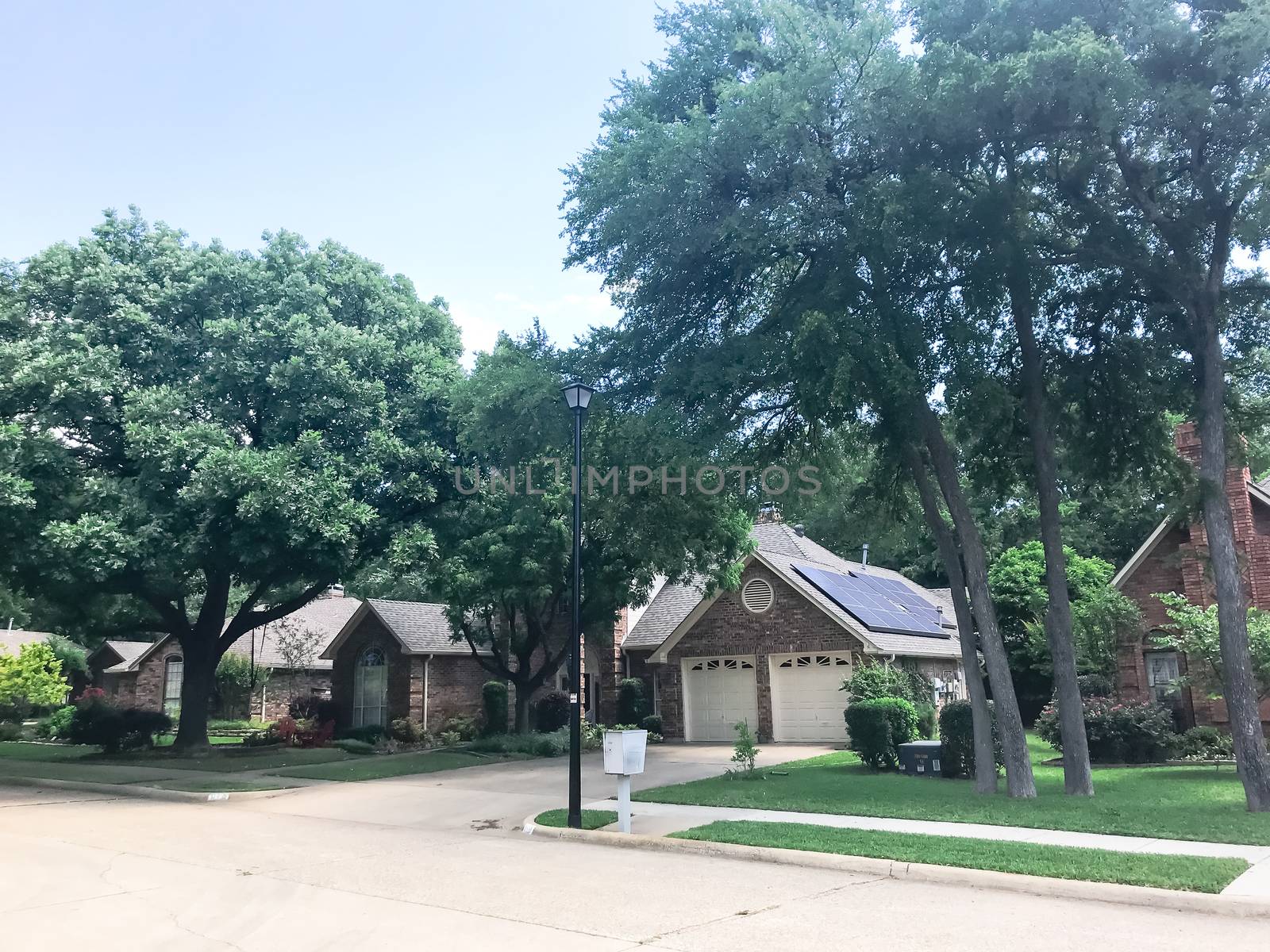 Front porch entrance of typical residential house in suburban Dallas, Texas, America with solar panel on shingle roof surrounds by tall oak and pine trees.