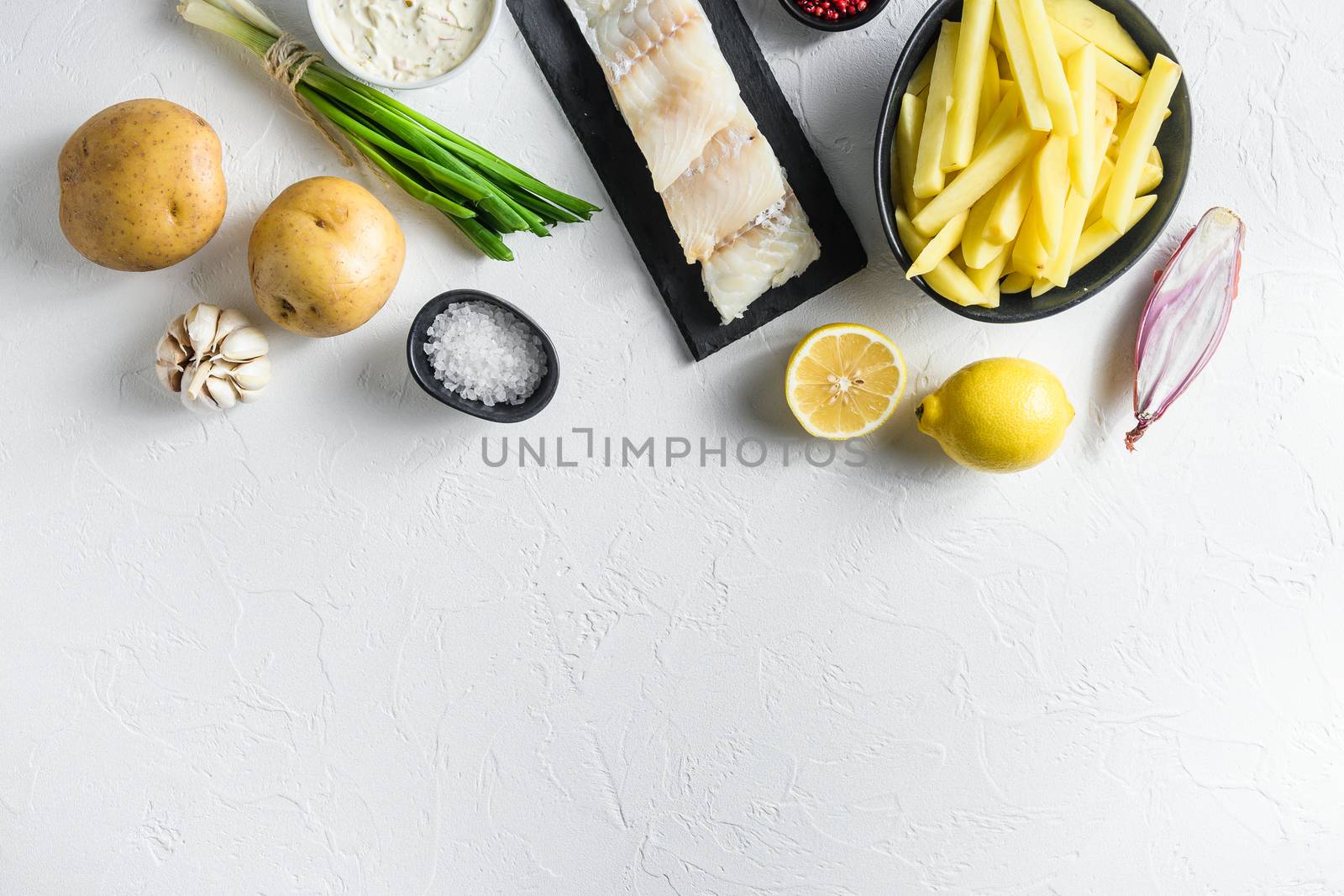 Traditional fish and chips ingredients recipe raw cod fillets on stone slate batter, potatoe, tartar sauce, lemon, capers , green herbs garlic, salt, peppercorns on white stone background top view concept in raw space for text on bottom by Ilianesolenyi