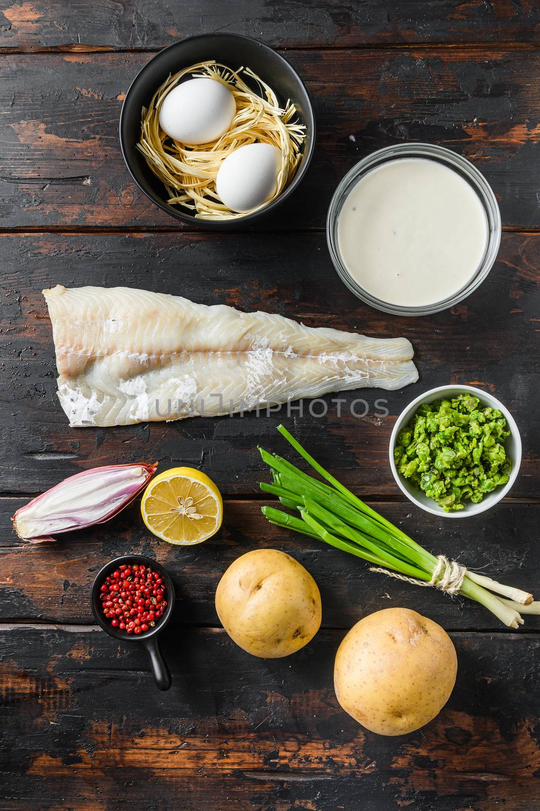 Organic fish and chips ingredients white fish fillet beer batter, potatoe, tartar sauce, minty mushy peas, lemon , shallot, mint, garlic, salt, peppercorns on rustic old wood table top view vertical.