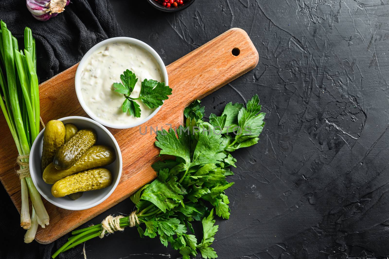 Homemade Tartar Sauce with organic ingredients pickles, capers, dill, parsley, garlic, lemon and mustard on a dark black stone concrete background. Horizontal, top view space for text.