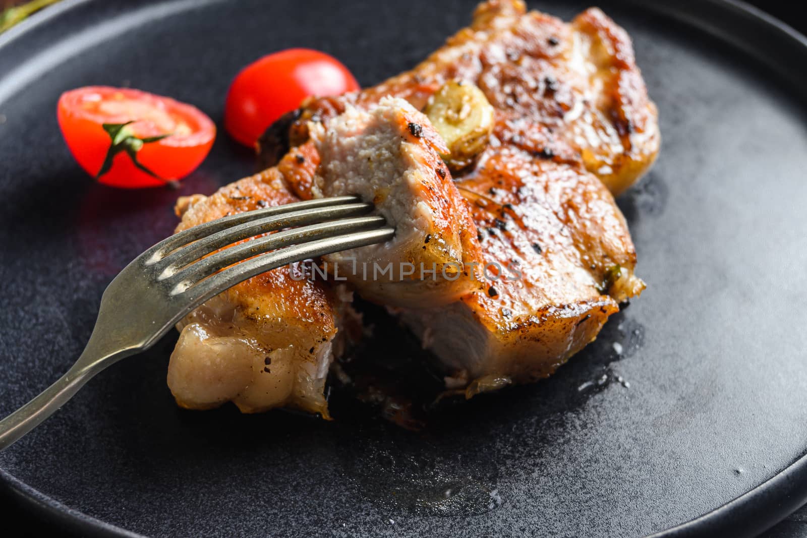 Dish of grilled pork chop with tomatoes top view with knife and slice on fork over old rustic dark wood table table close up new wide angel. High quality photo