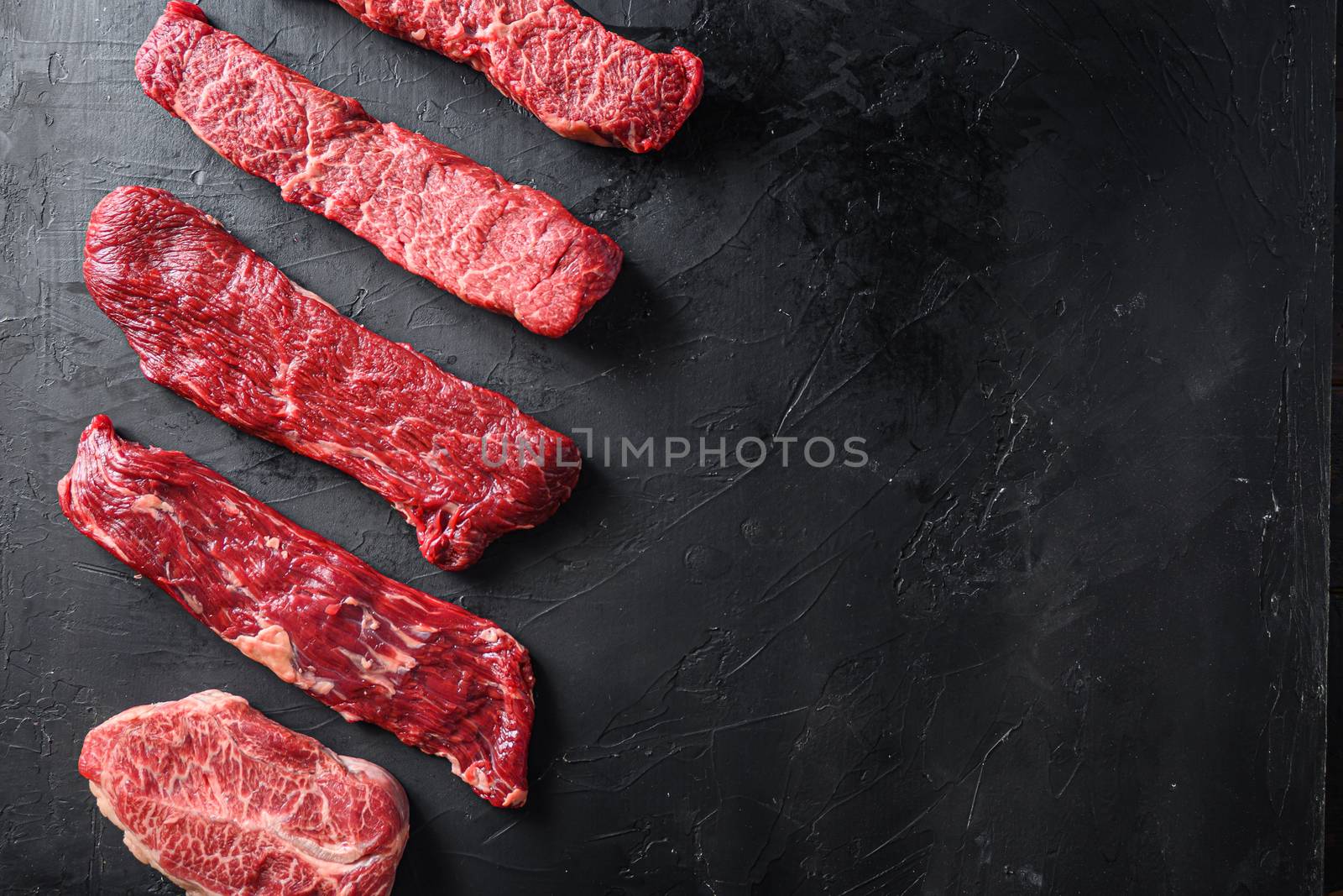 Raw, alternative beef steaks flap flank Steak, machete steak or skirt cut, Top blade or flat iron beef and tri tip, triangle roast with denver cut . Black stone background. Top view. Space for text by Ilianesolenyi